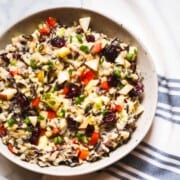 Curried Wild rice salad in a speckled bowl sitting on a white marble next to a white with blue striped dish cloth