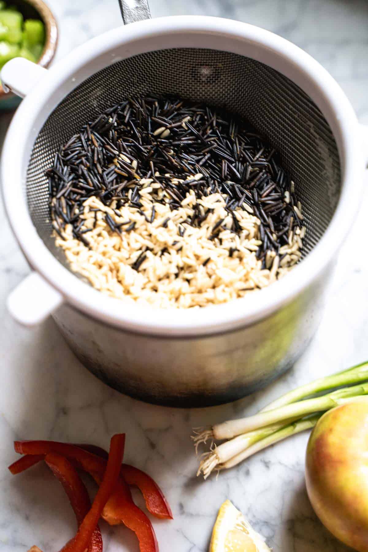 Rinsed Wild rice and brown rice in a fine mesh sieve over a pot.