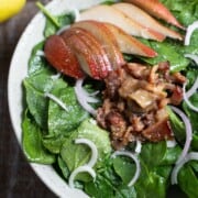 Apple spinach salad with warm bacon maple dressing in a bowl on a wooden table.