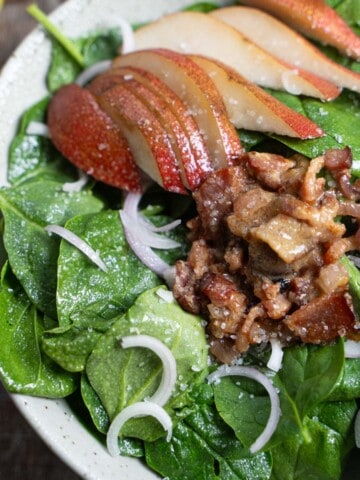 Apple spinach salad with warm bacon maple dressing in a bowl on a wooden table.