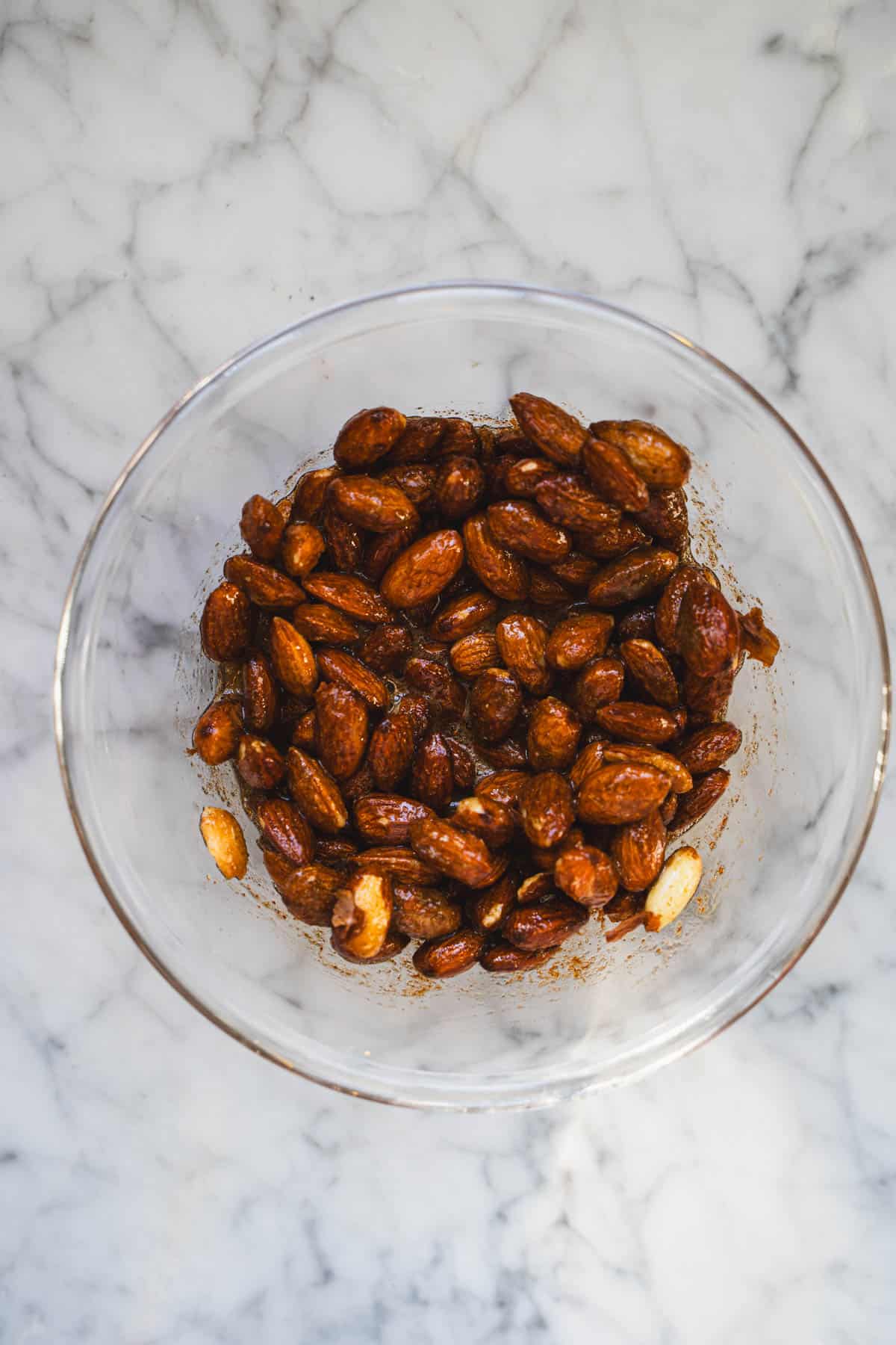 Nuts coated with spices in a glass bowl on a marble counter.