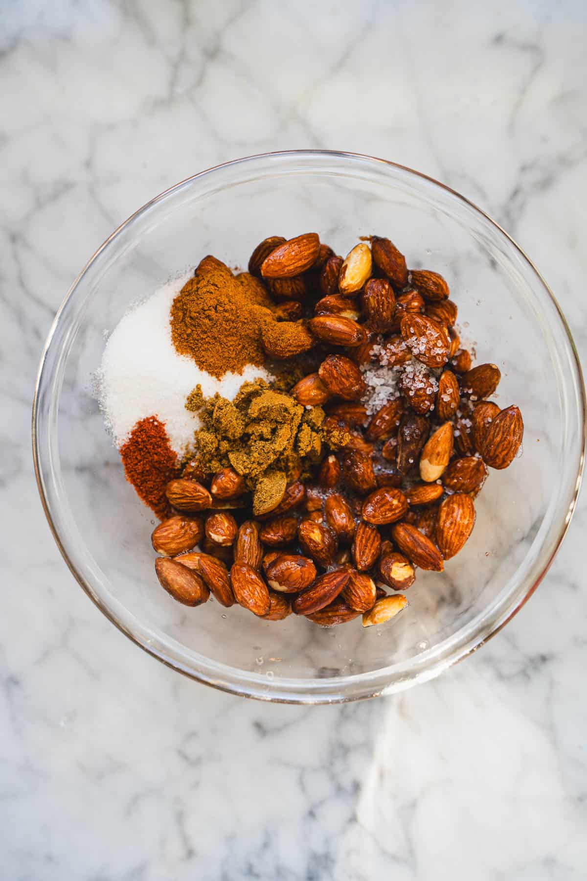 sweet and spicy nuts ingredients in a clear glass bowl sitting on white marble counter