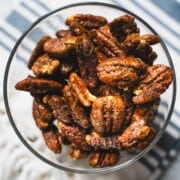 Sweet and Spicy Nuts in a glass bowl sitting on top of a blue striped dish towel