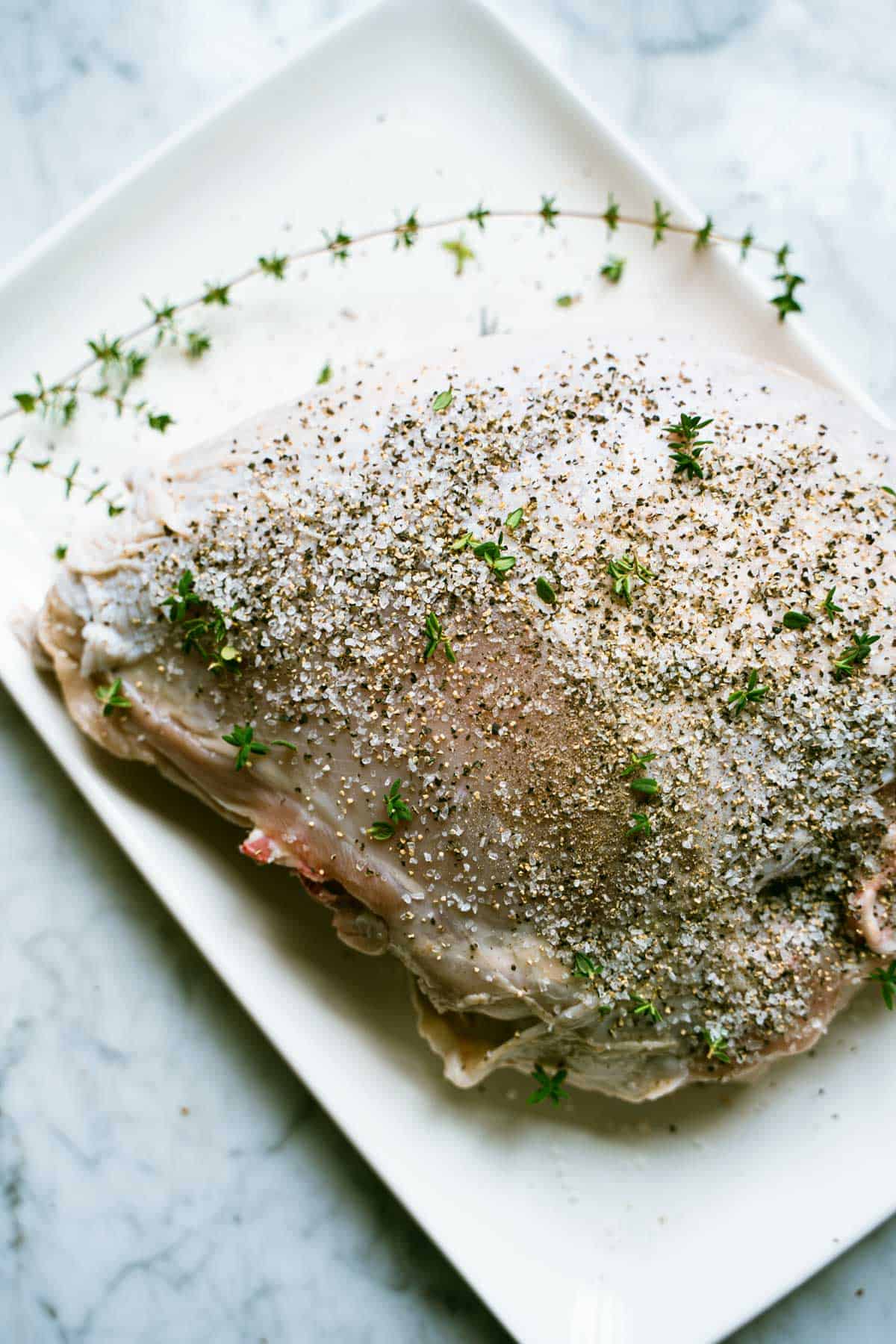 Turkey breast on a large plate sprinkled with salt, pepper and thyme.