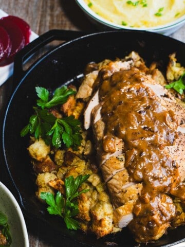 Turkey breast placed on top of stuffing in one pan, surrounded by bowls of traditional sides on a wood table.