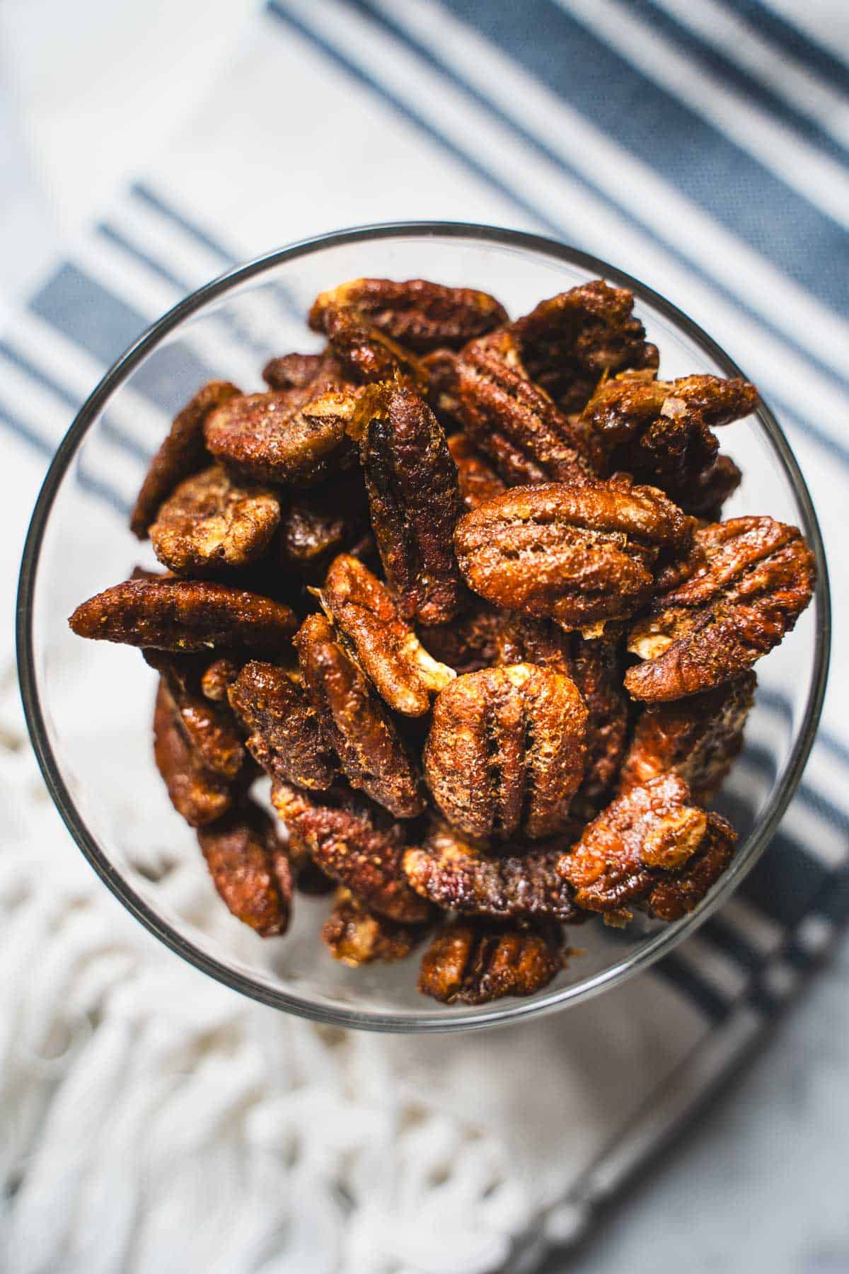 Sweet and Spicy Nuts in a glass bowl sitting on top of a blue striped dish towel