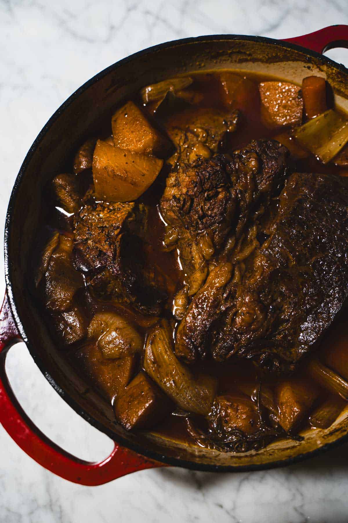 Tender 2 lb pot roast for two fully cooked resting in a dutch oven on a white marble counter.
