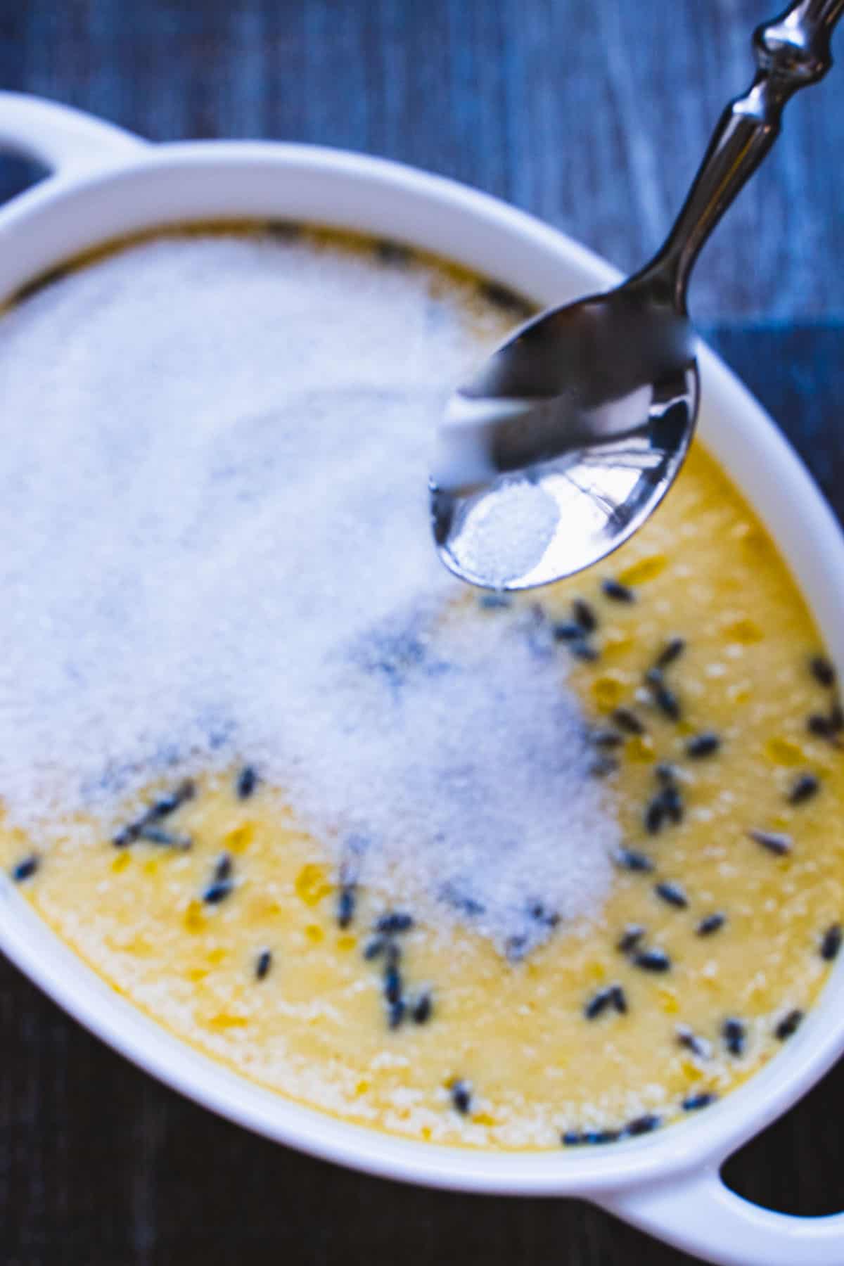 Sugar being sprinkled over the top of a baked creme brulee with a spoon.