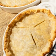 Easy homemade individual chicken pot pie on brown cutting board set on top of a white kitchen towel with blue strips.