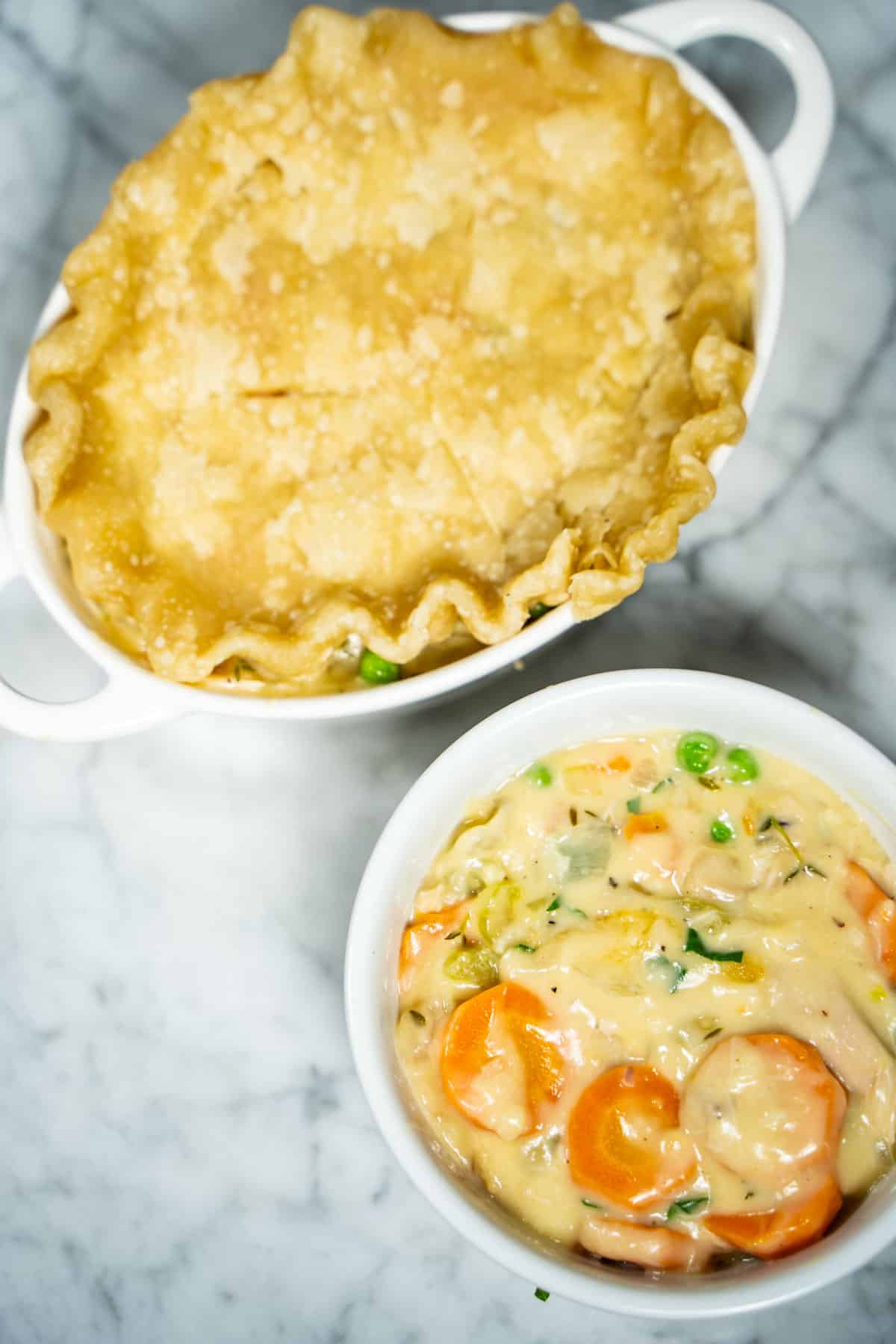 2 pot pies on white marble counter. One is fully assembled with crust on top the other ramekin has 2 cups filling in it.