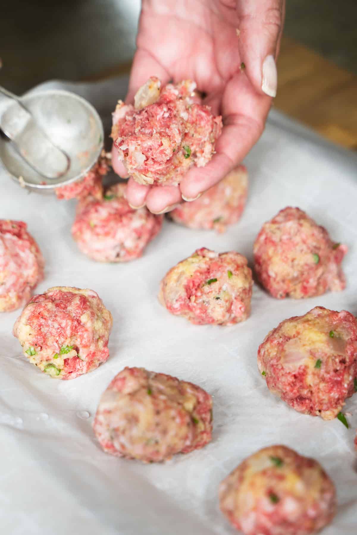 Golf ball sized meatballs on a baking sheet lined with parchment paper.