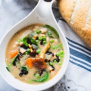 Creamy 10 vegetable and bean soup without tomatoes or cream in a white bowl on a table next to the dutch oven.