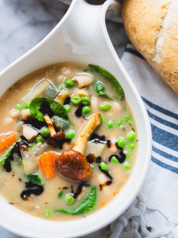 Creamy 10 vegetable and bean soup without tomatoes or cream in a white bowl on a table next to the dutch oven.
