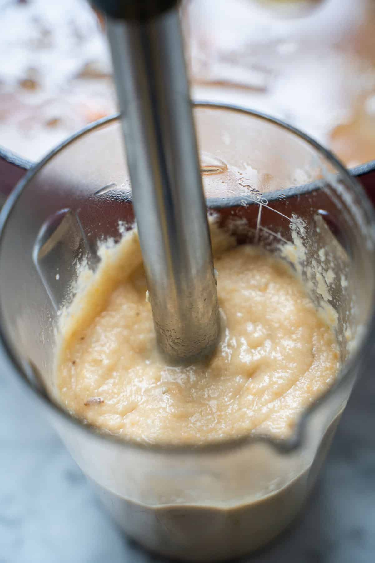 Immersion blender pureeing soup base in a  immersion blender beaker.