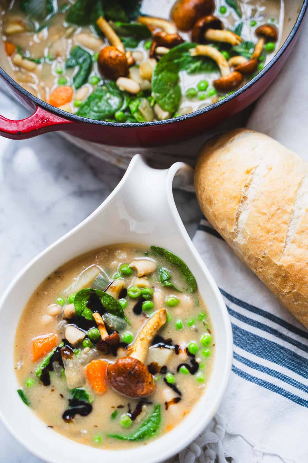 Creamy 10 vegetable and bean soup without tomatoes or cream in a white bowl on a table next to a loaf of bread.