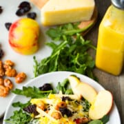 Honey Citrus Champagne Vinaigrette Salad Dressing in a vinaigrette glass bottle with a pour spout sitting next to an arugula salad and salad ingredients.