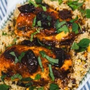 one pot glazed apricot harissa chicken breasts and pearl couscous on a white serving platter sitting on top of blue stripped dish towels.