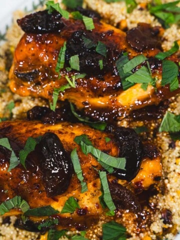 one pot glazed apricot harissa chicken breasts and pearl couscous on a white serving platter sitting on top of blue stripped dish towels.