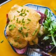 Irish eggs benedict with corned beef, sauerkraut and pouched eggs on english muffin topped with easy hollandaise sauce on a orange plate.