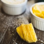 Old fashioned lemon pudding cake in a dessert cup sprinkled with powdered sugar and a spoon ful of cake on a wooden table.