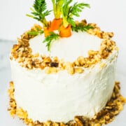 Cream cheese frosted carrot walnut cake with chopped walnuts on edges and fresh carrot tops on top of the small 6-inch 2- layer cake.