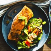 Sweet and spicy pepper glazed salmon served with a mixed green salad tossed in a pepper jam vinaigrette on a blue plate.