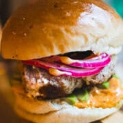 Turkey Burger topped with gochujang mayo, avocado pickles and red onion on a wooden board.
