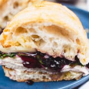 turkey and cheese with arugula rocket and spiced blueberry sandwich on a ciabatta bun sitting on a blue plate.