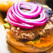 Turkey avocado burger with gochujang mayo and toppings layered on a White bun sitting on a wood board.