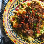 Sausage and bell pepper pasta using plant based sausage and alfredo sauce in a yellow and blue pasta bowl resting on a white napkin with blue horizontal strips.