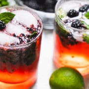 Two old-fashioned glassed filled with muddled blackberries and mint with ice cubes and garnished with mint for a valentines day cocktail.