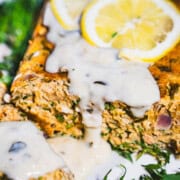 Gatsby Salmon Loaf with champagne white sauce and slices of lemon on a bed of dill on a white platter.