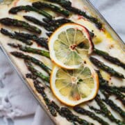Lazy ravioli lasagna topped with white sauce white and garnished with asparagus tips and 2 slices of lemon in a loaf pan.