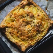 Savory potato parmesan puff pastry tart on a parchment lined baking sheet.