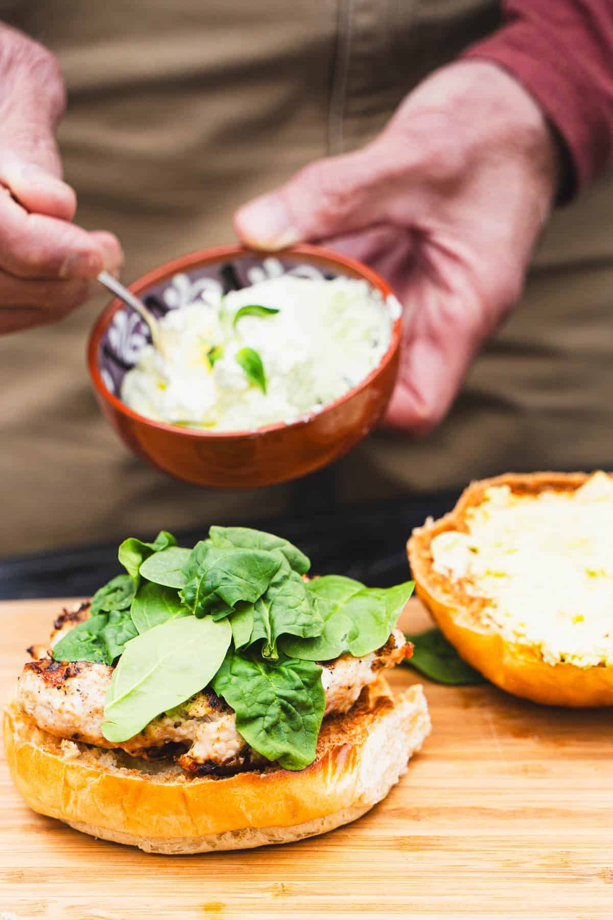 whipped feta spread being slathered onto the top of a hamburger bun for a greek feta spinach chicken burger