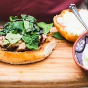 Greek feta spinach chicken burger on a wooden cutting board held by a person with a maroon shirt.