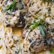 Sheet pan chicken thighs with fresh tarragon surrounded by white onions and a tarragon cream sauce on a white platter.