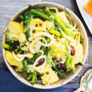 Green bean and potato Salad with thinly shaved fennel, basil and olives in a brown marble bowl sitting on a blue napkin.
