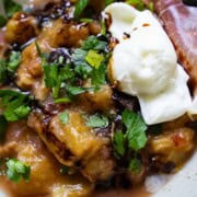 Agrodolce sauce with rhubarb, cipollini and dried cherries topped with burrata and a thin slice of prosciutto garnished with parsley in a green brown specked bowl.