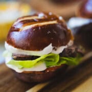Beef tenderloin with horseradish sauce on pretzel slider bun with lettuce on a wooden board.