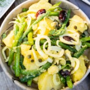 Green bean and potato Salad with thinly shaved fennel, basil and olives in a brown marble bowl sitting on a blue napkin.