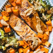 Miso butter salmon and roasted sweet potatoes and broccoli on a white platter garnished with creamy miso sauce.