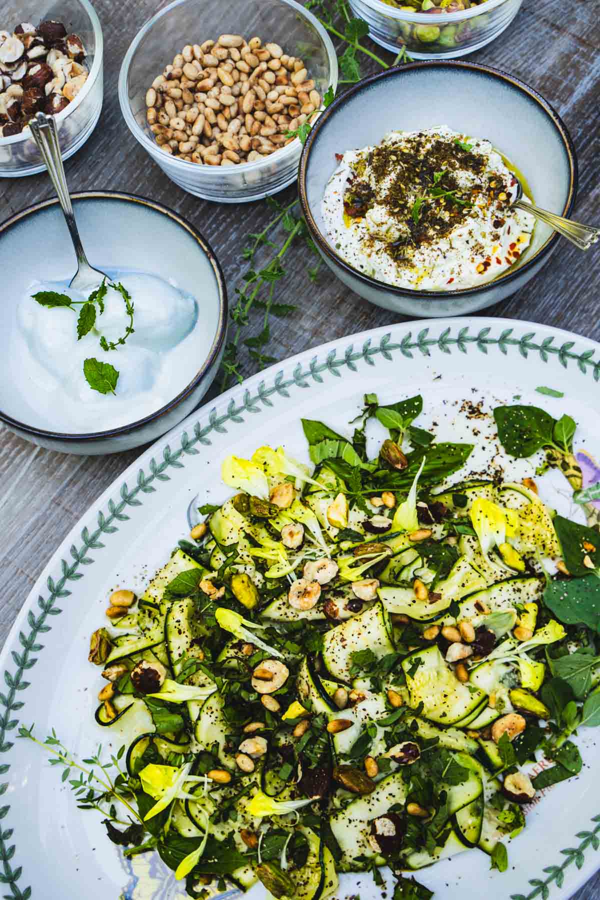 Raw Italian Zucchini salad on a white plate next to bowls of burrata and ricotta dressed with zaatar and olive oil.
