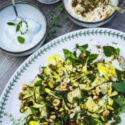 Raw Italian Zucchini salad on a white plate next to bowls of burrata and ricotta dressed with zaatar and olive oil.
