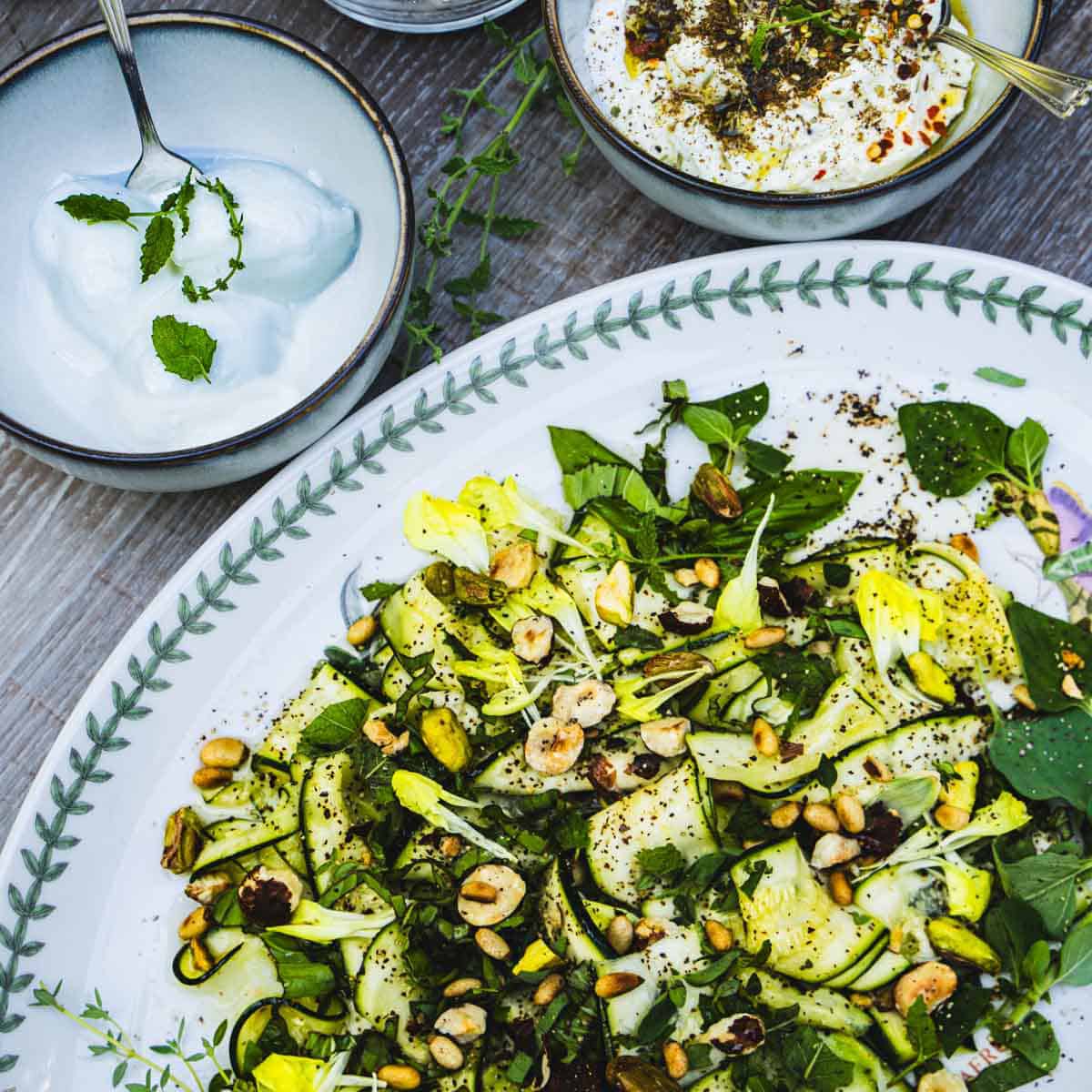 Raw Italian Zucchini salad on a white plate next to bowls of burrata and ricotta dressed with zaatar and olive oil.