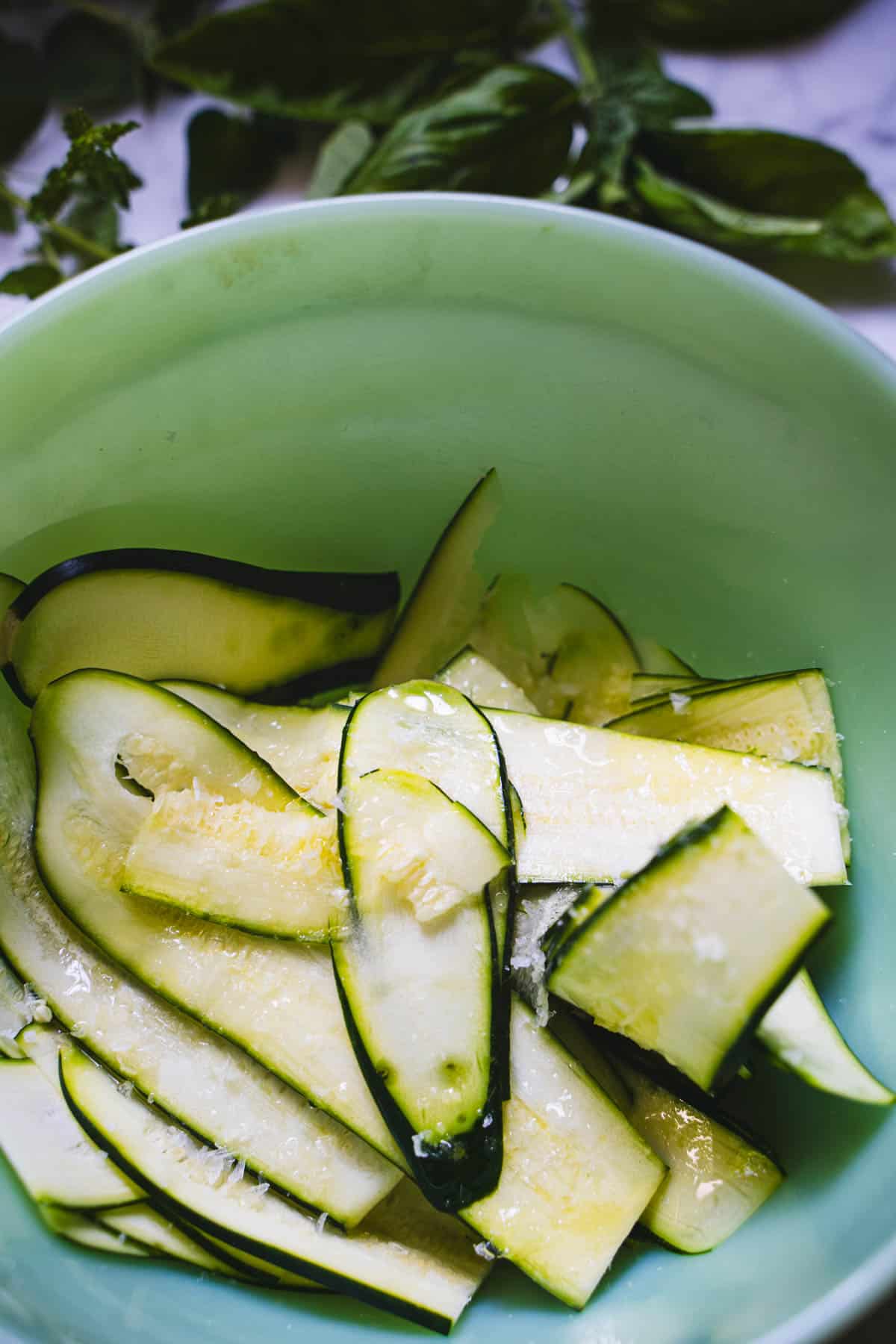 Ribbons of Zucchini placed in a green bowl sprinkled with hazelnut oil, vinegar and salt.