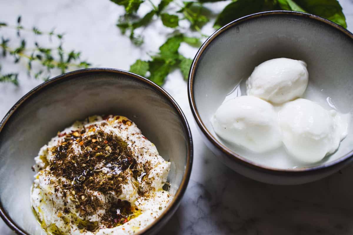 One bowl of ricotta sprinkled with Za'atar, and olive oil and one bowl with buratta.