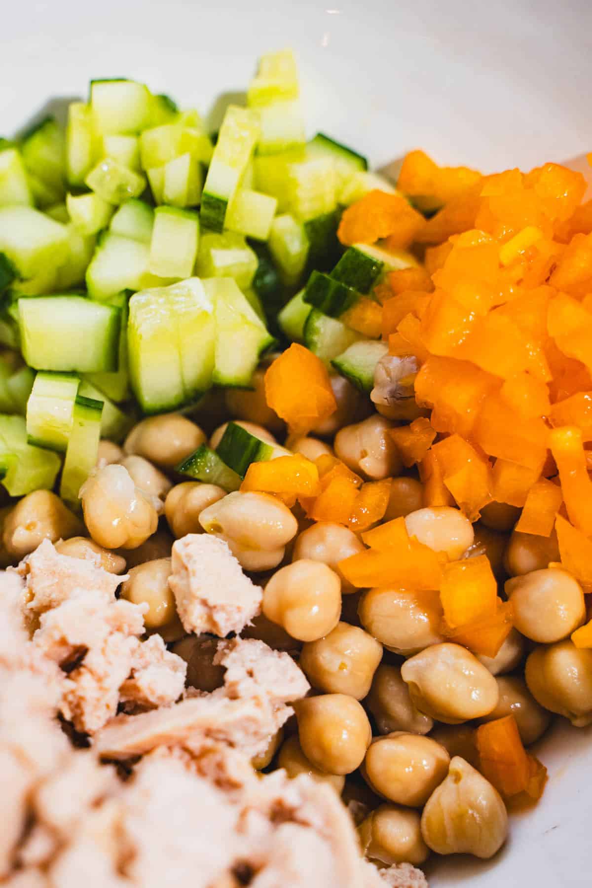 Ingredients for kale, cucumber, chickpea, pepper and tuna salad in a white salad bowl.