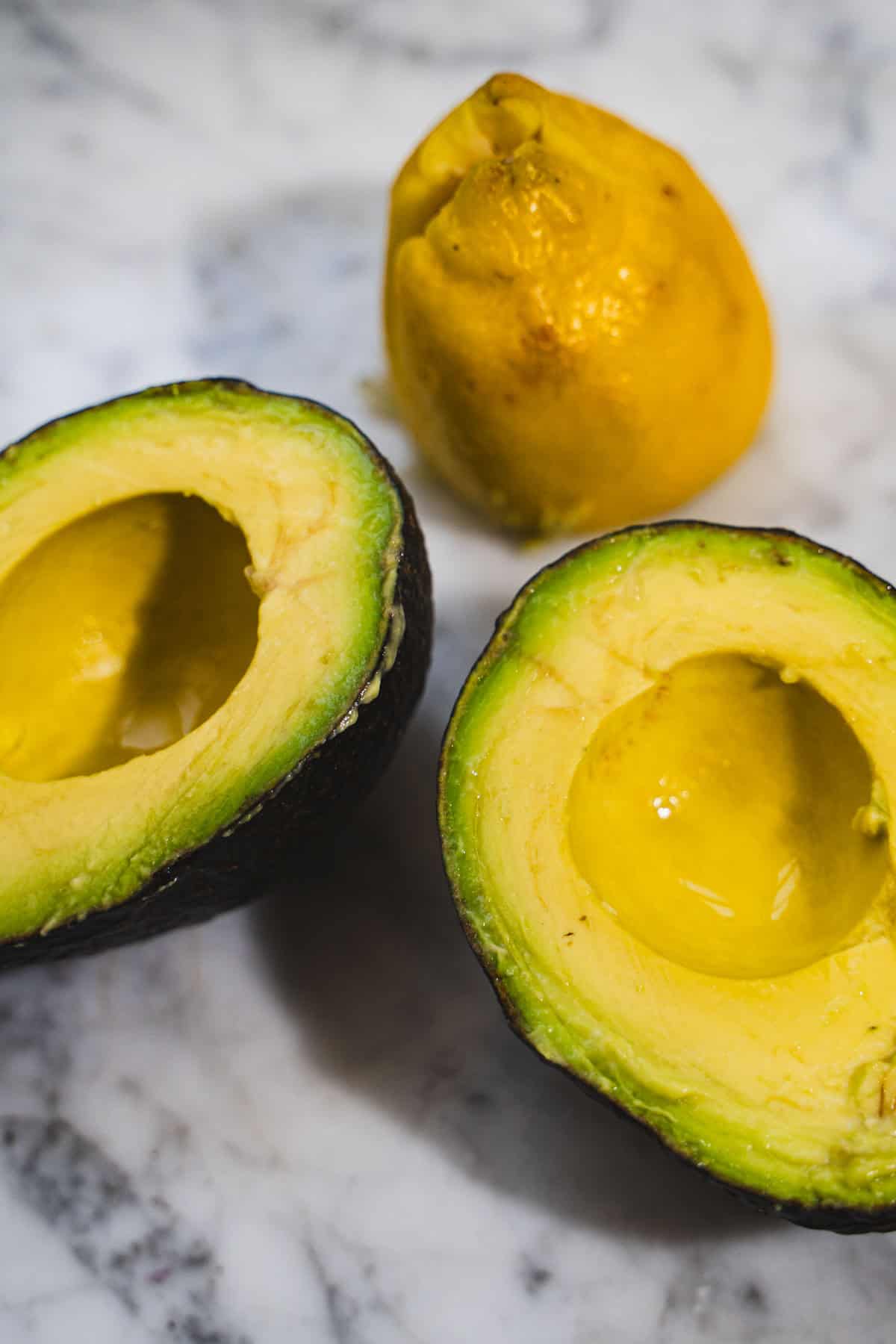 Large avocado split in half with pit removed resting on a white marble counter top ready to be stuffed.