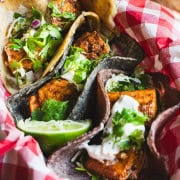 Three Mahi mahi fish tacos with cabbage slaw in a red and white checked basket garnished with cilantro and cilantro lime sauce for fish tacos.